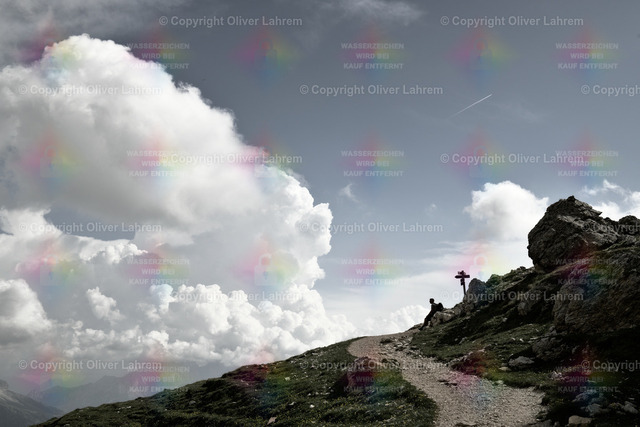 Der ruhende Wanderer | Ein Wanderweg führt zu einer Wegkreuzung in den Bergen, und die Silhouette eines sitzenden Wanderers unter einem Wegweiser vor einem blauem Himmel mit Cumulus Wolken 